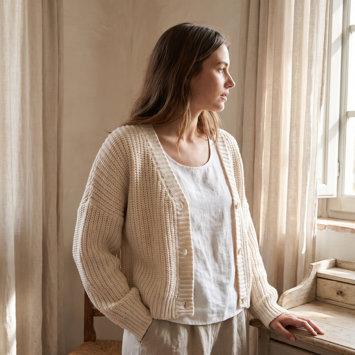 Cardigan donna corto in maglia grossa crema indossato in un ambiente luminoso